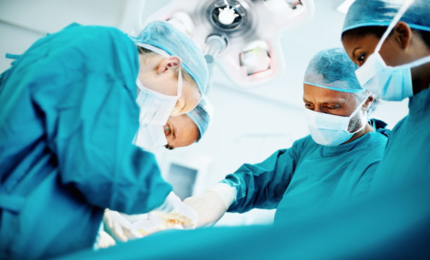 Photo of surgery being performed in operating room, shows intent concentration on team's faces.